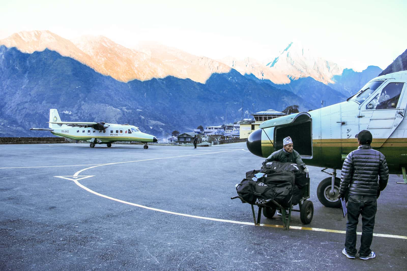 A man loads a small plane with trekking bags at the tiny, mountain backed Lukla airport Nepal - the start of the Everest Base Camp Trek