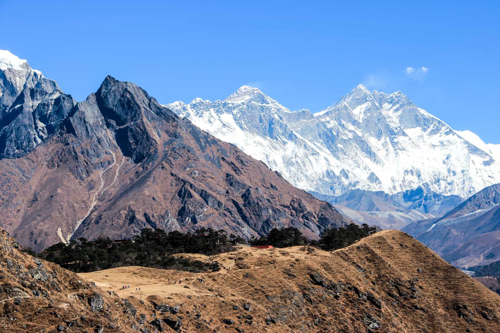 Layers of the Himalaya mountains - a light brown ledge and behind a dark brown mountain peak and a snow-capped mountain peak