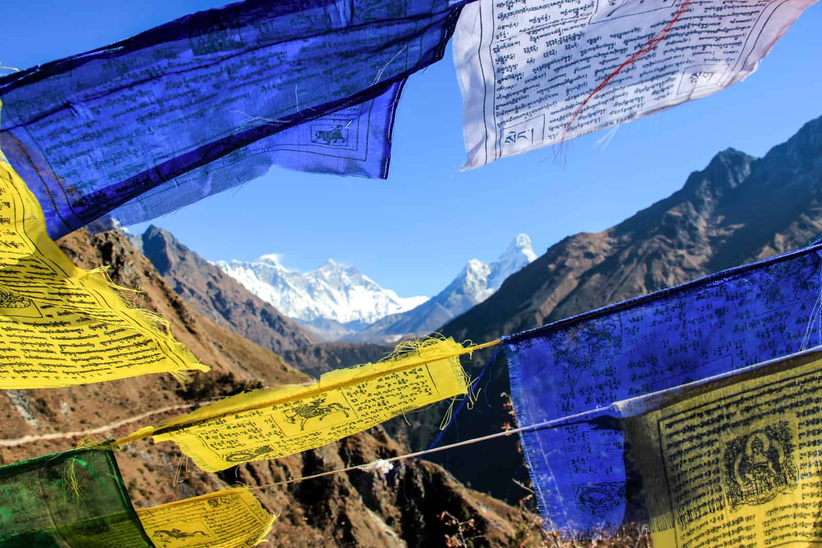 Blue, yellow and white prayer flags blowing in the wind in front of a mountain landscape.