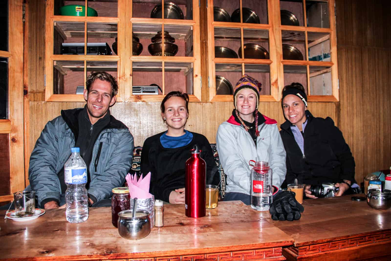 Four people, dressed in trekking gear, sit at a table in a traditional wooden-built Nepali teahouse found on the Everest Base Camp trek in the mountains