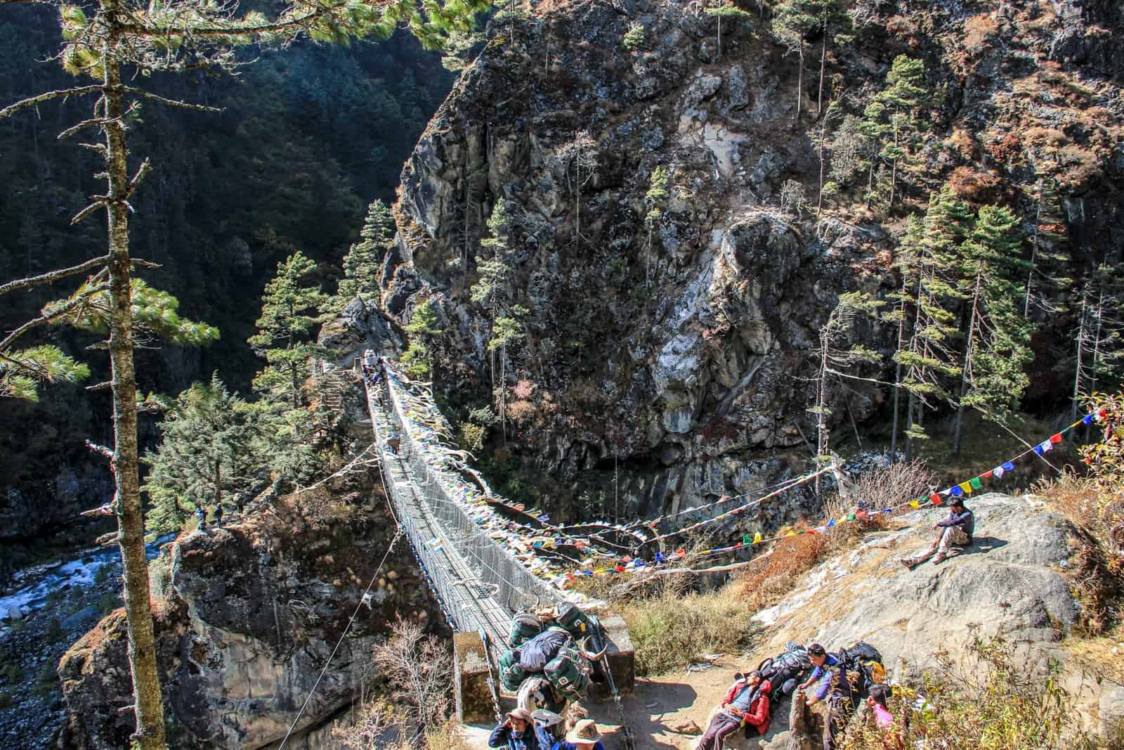 Trekkers rest on rocks by the start of a metal suspension bridge crossing on the Everest Base Camp Trek 