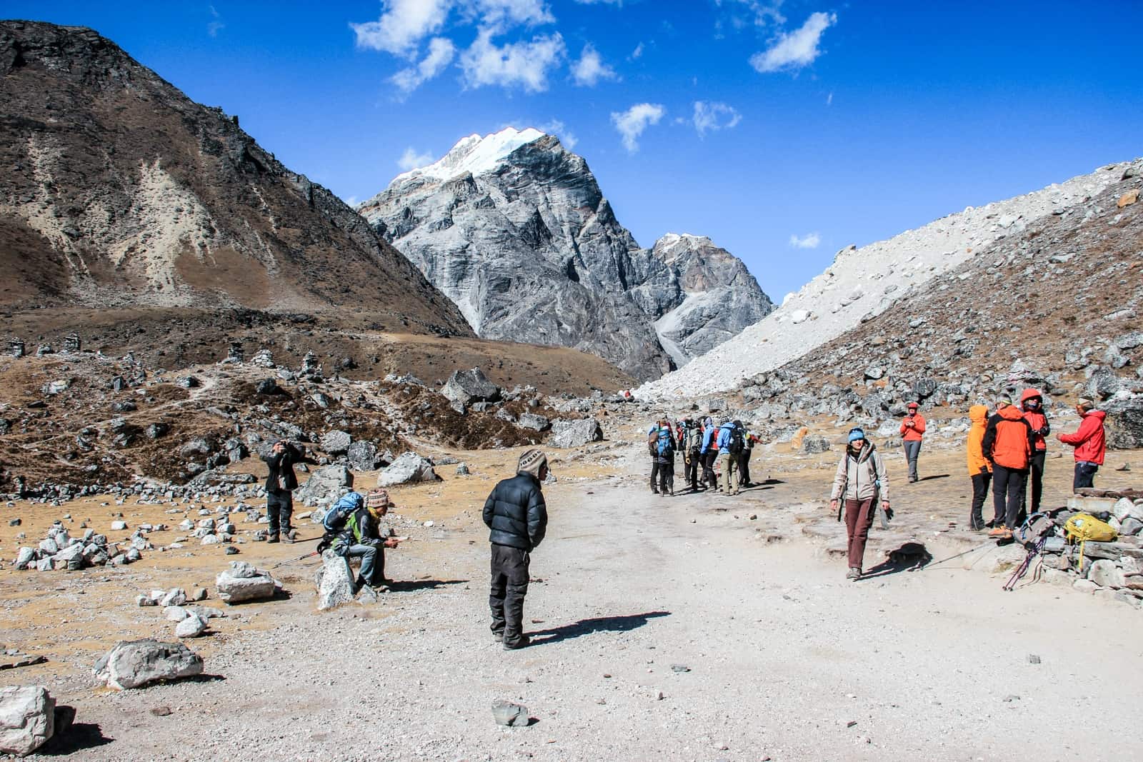 A small group of trekkers stand in the wide open valley between mountain faces in the Himalayas of Nepal