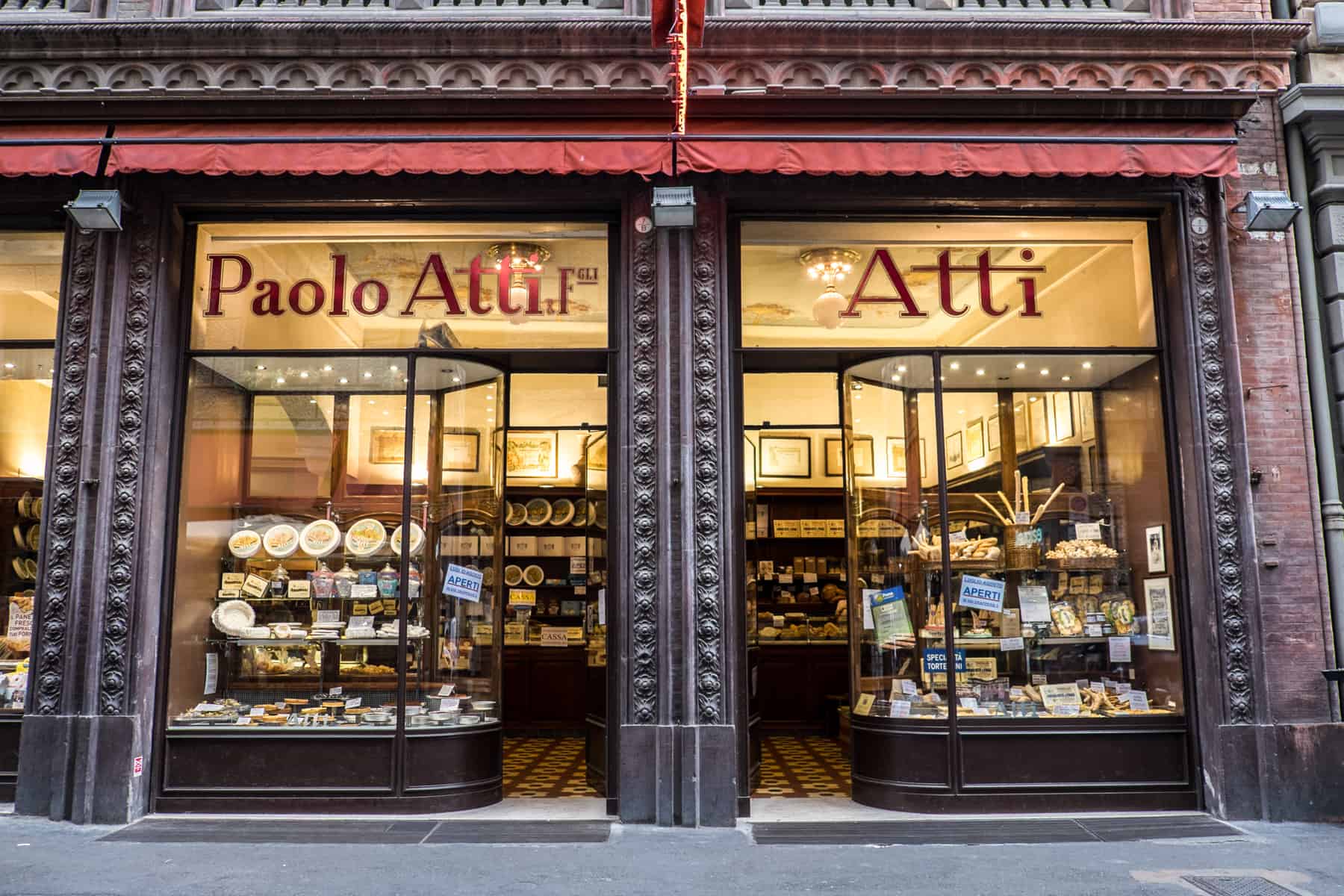 A glass fronted, dark wooden panelled store front filled with food goods, with the words: "Paolo Atti. F. Atti" overhead. 