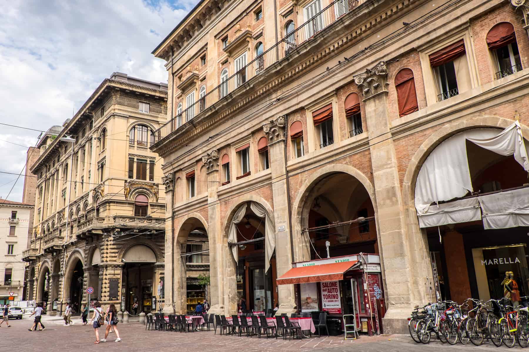 A tall and wide golden brown structure with Renaissance architecture columns, archways and decorative balcony in Bologna's Piazza Maggiore. 