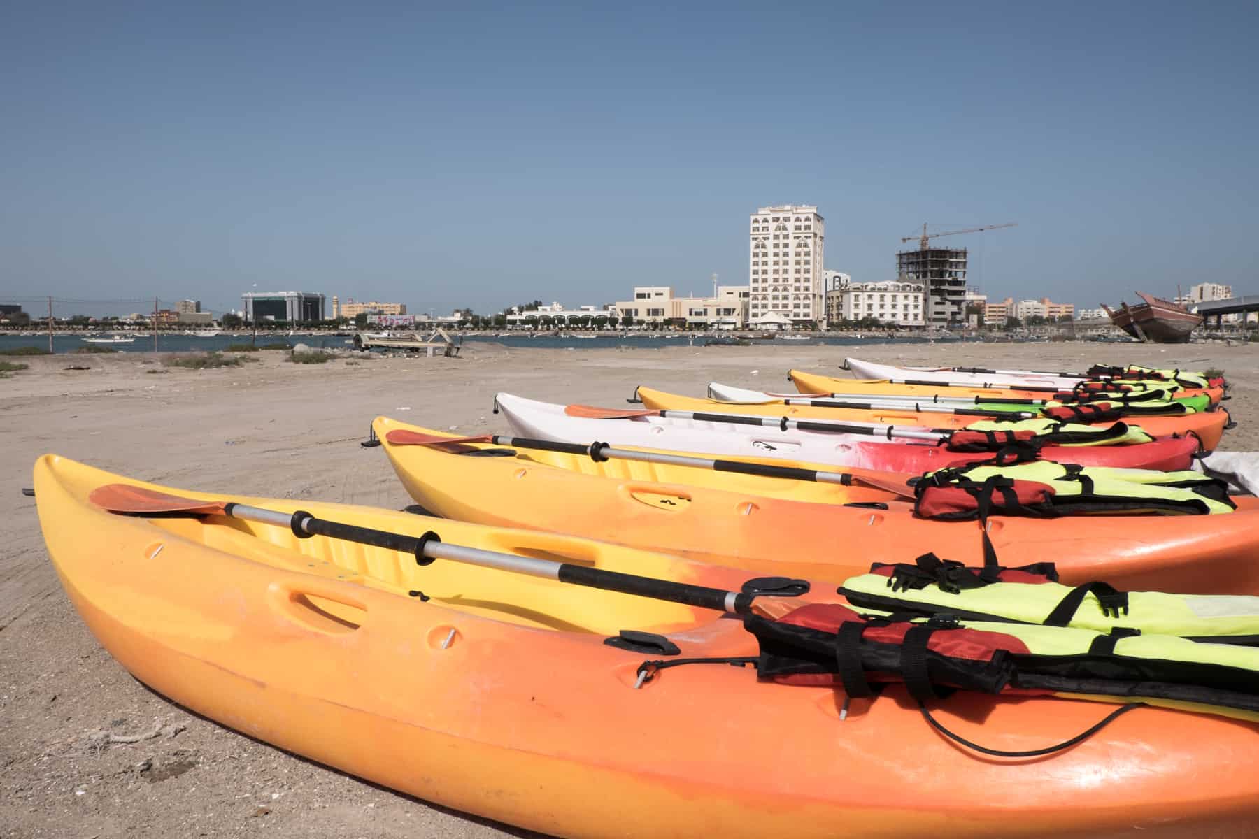 A row of seven orange and white kayaks on a sand beach next to a body of water in the city of Ras Al Khaimah in the UAE