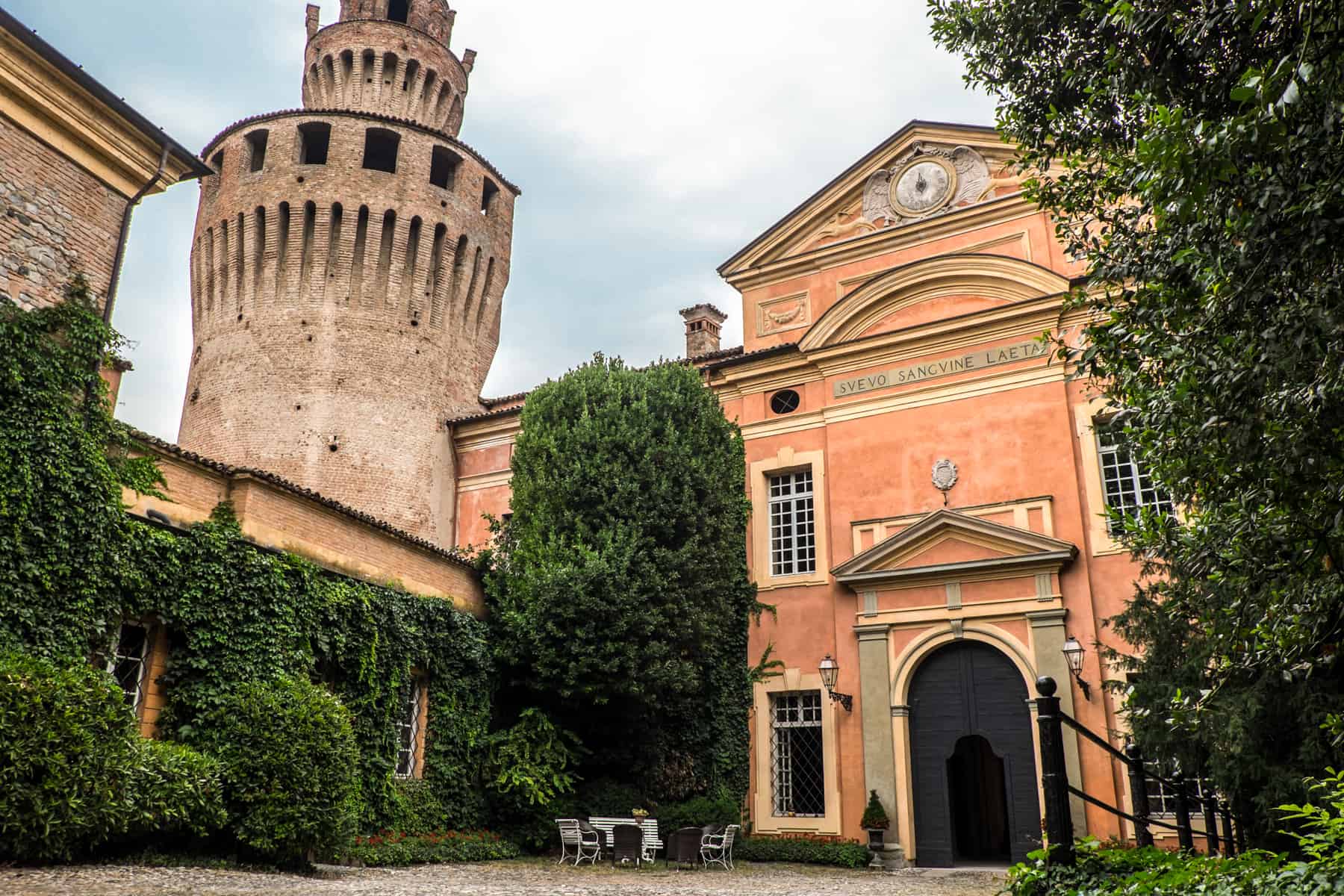 A triangular roofed orange manor house building that connects with a medieval stone castle tower in Piacenza, Italy. 