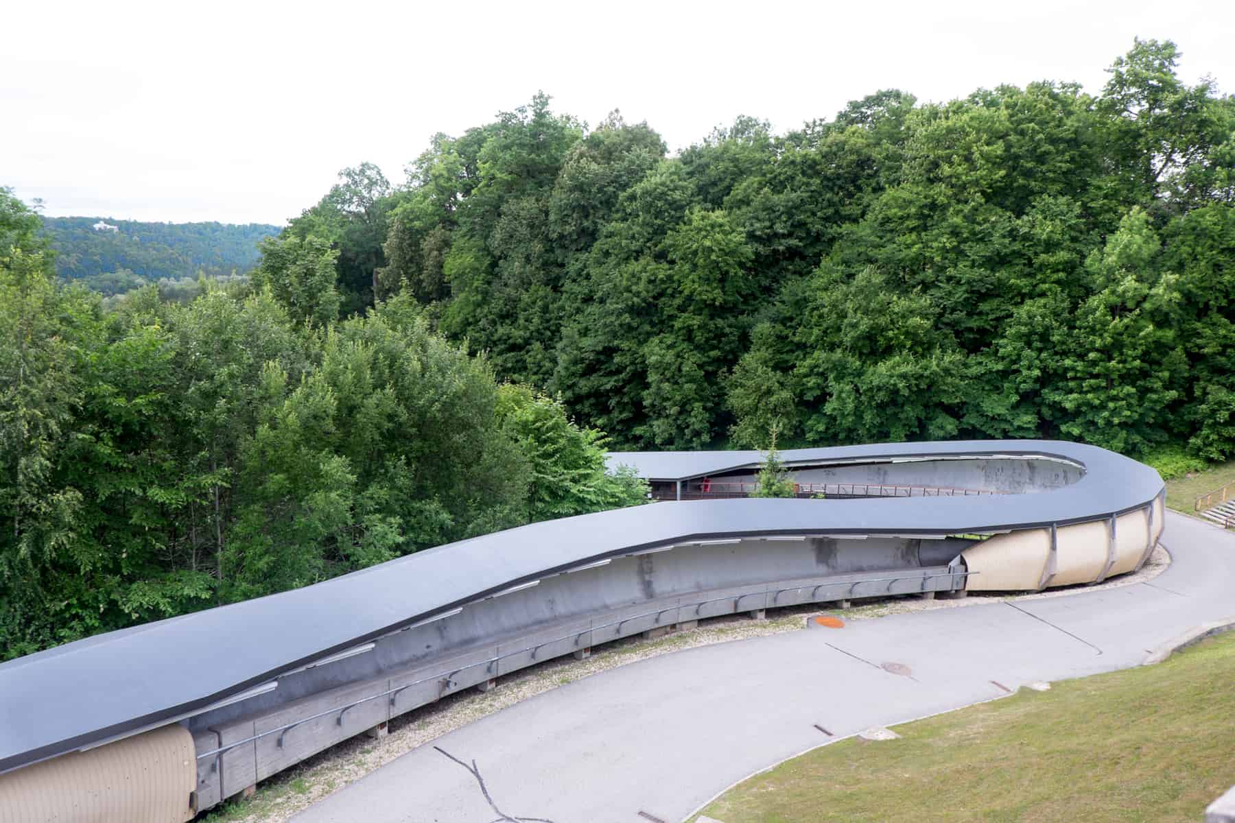 A grey looped tunnel curves left and towards between two lanes of trees. it is the Olympic bobsleigh in Sigulda, Latvia