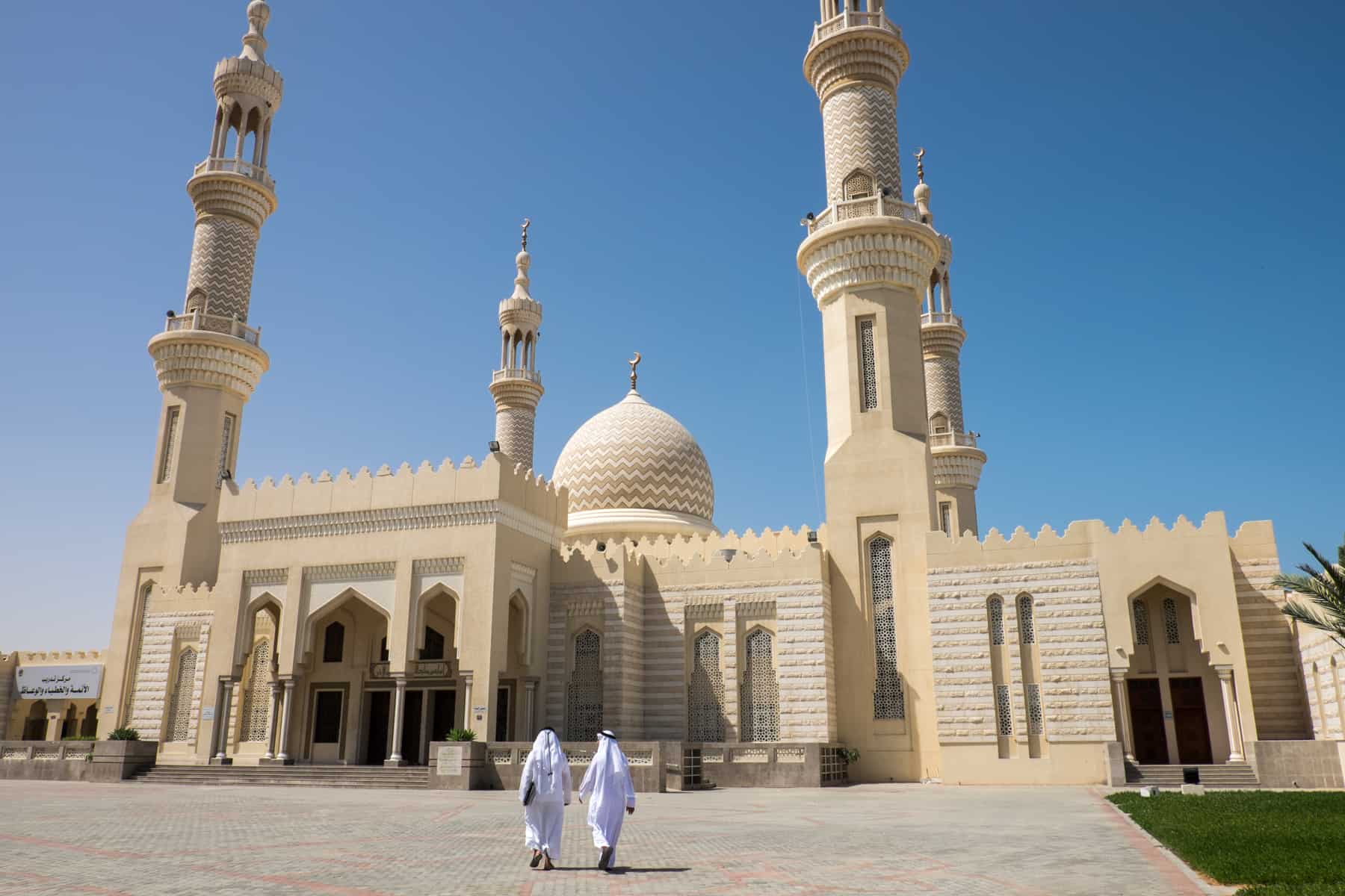 Two men in white approach the light yellow Shaikh Zayed Mosque in Ras Al Khaimah