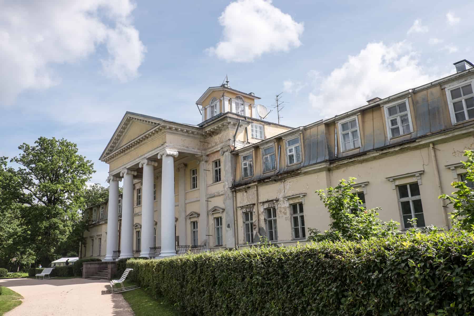 Krimulda Manor in Sigulda - a yellow neo-classical style building with white columns at the entrance, surrounded by manicured green hedges