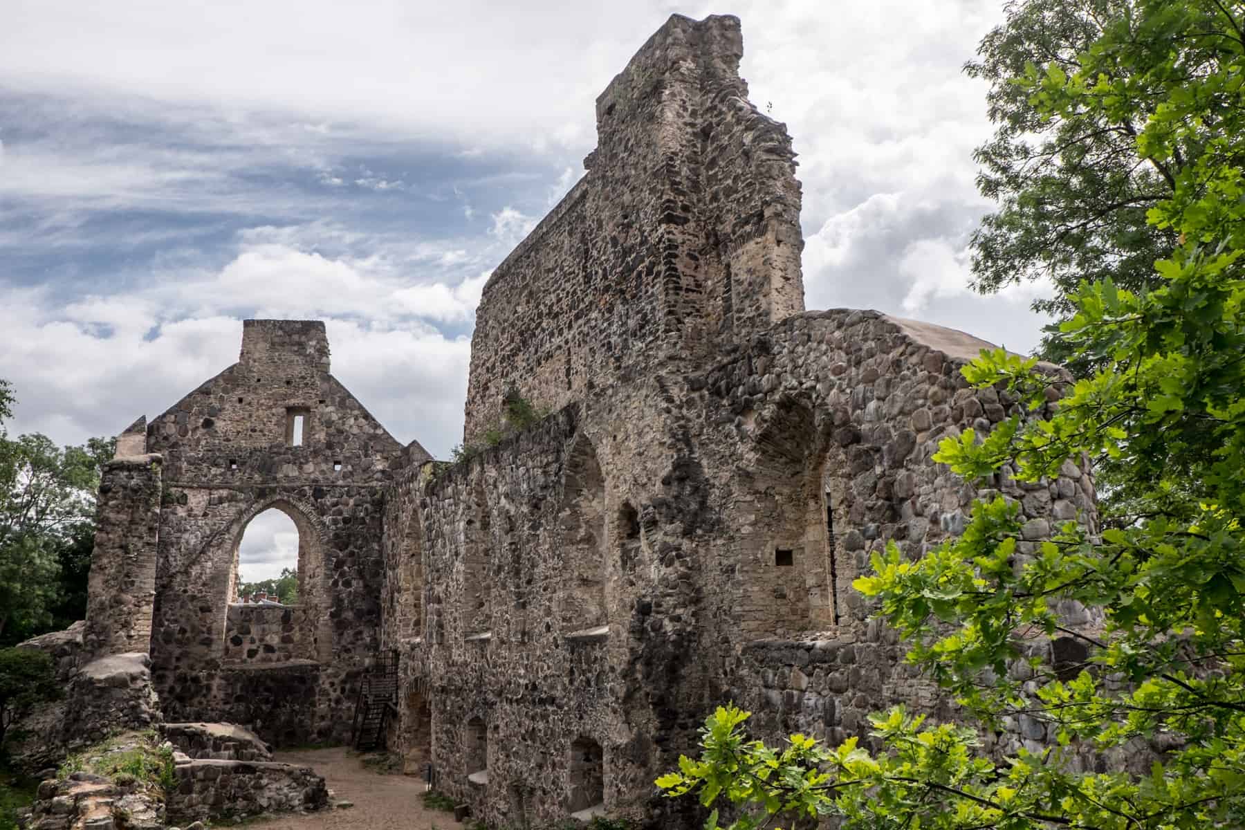 The tall greying ruins of a Medieval castle in Sigulda, Latvia, covered in nature.