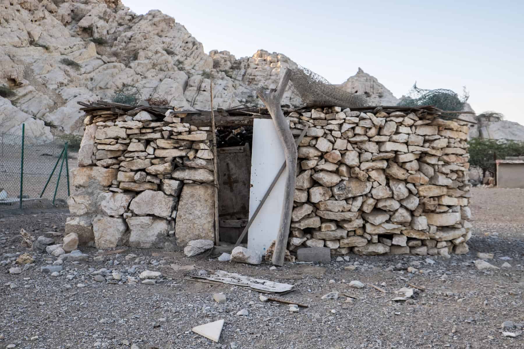 A small rectangular house made of surrounding mountain stone and a roof of tree branches.