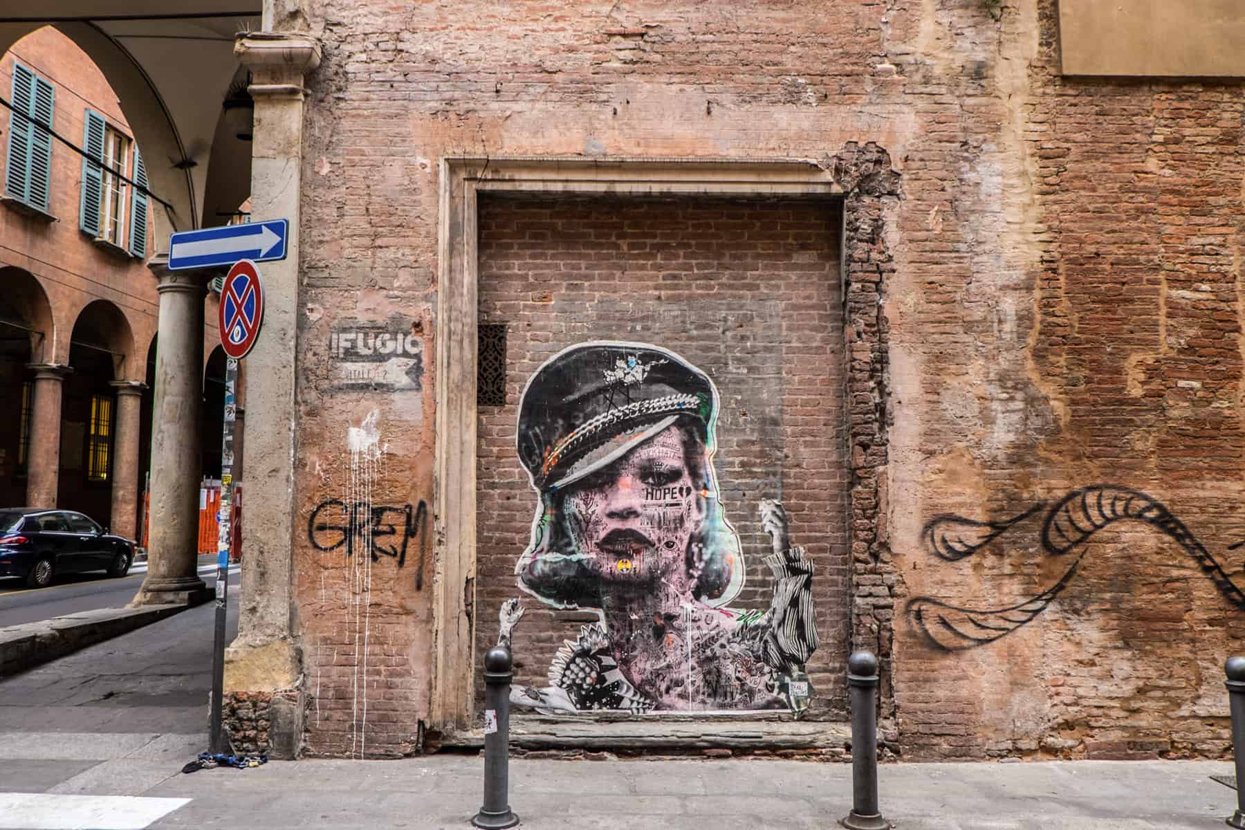 An orange-brown brick wall with paste up street art in Bologna, showing Kate Moss wearing a police hat. 