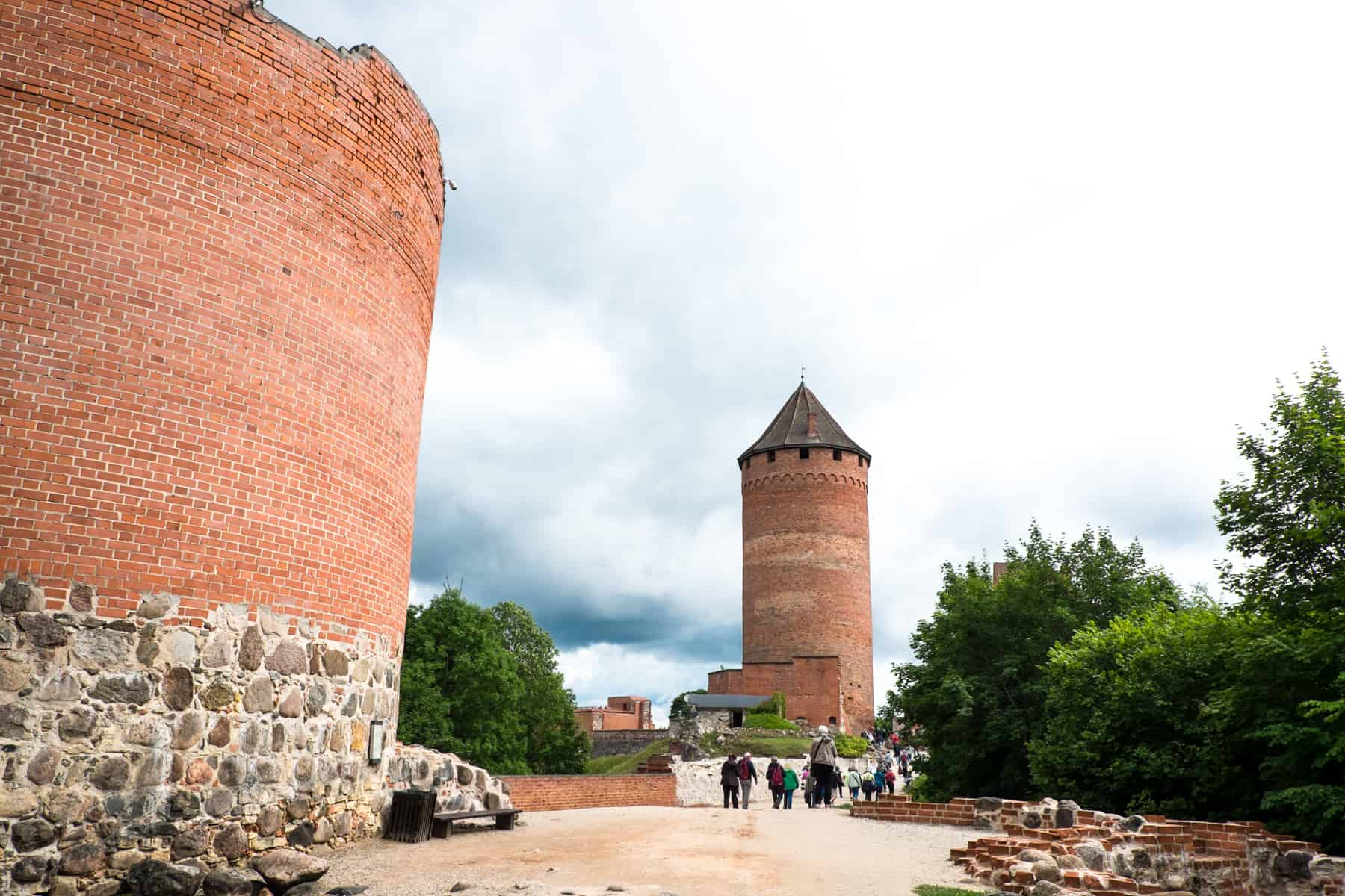 Two orange turrets, one with a silver pointed roof that people are walking towards, are the remains of Turaida Castle in Latvia.