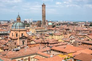 Elevated view of Bologna city over orange and yellow houses and the two stone towers that poke through.