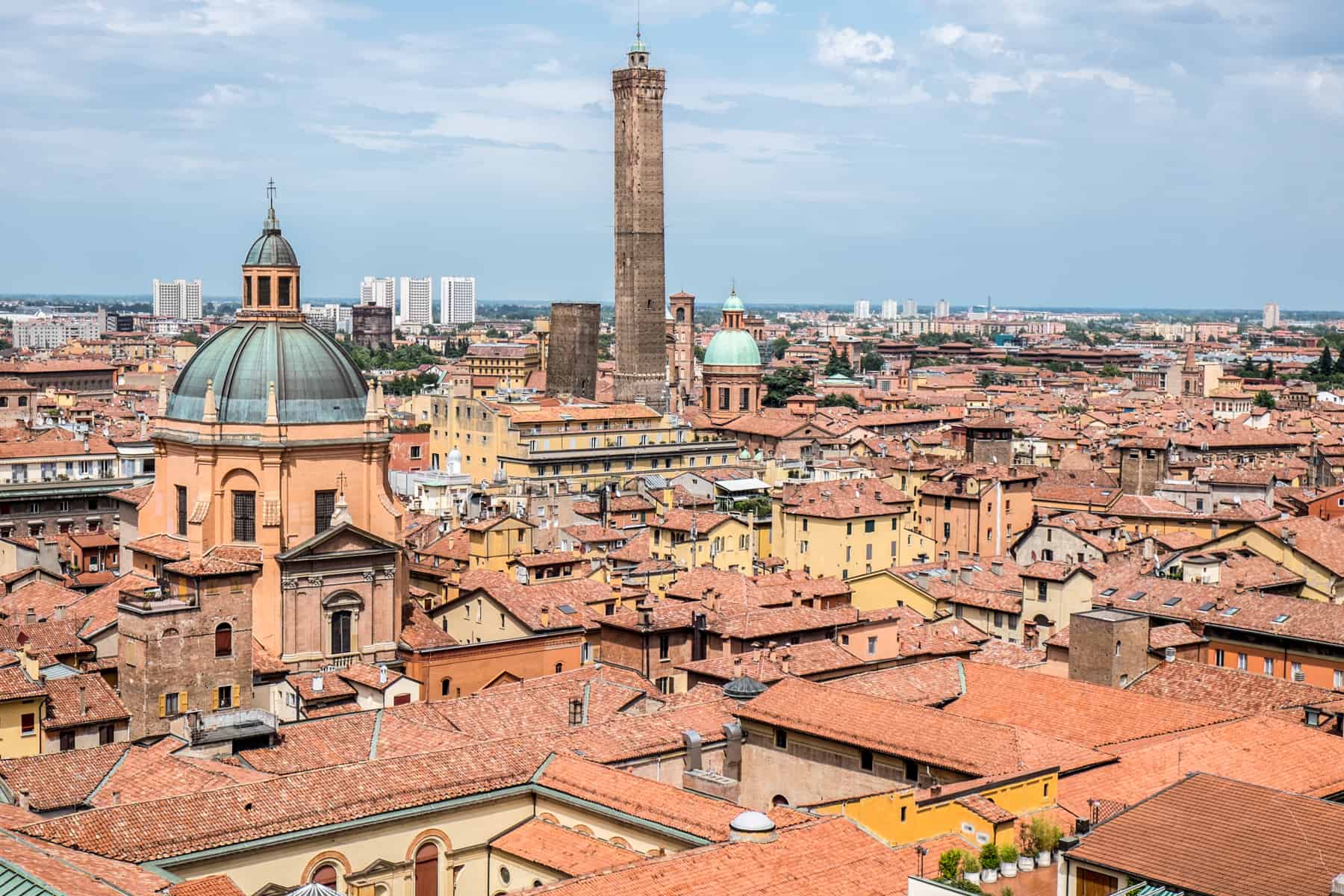 Elevated view of Bologna city over orange and yellow houses and the two stone towers that poke through.