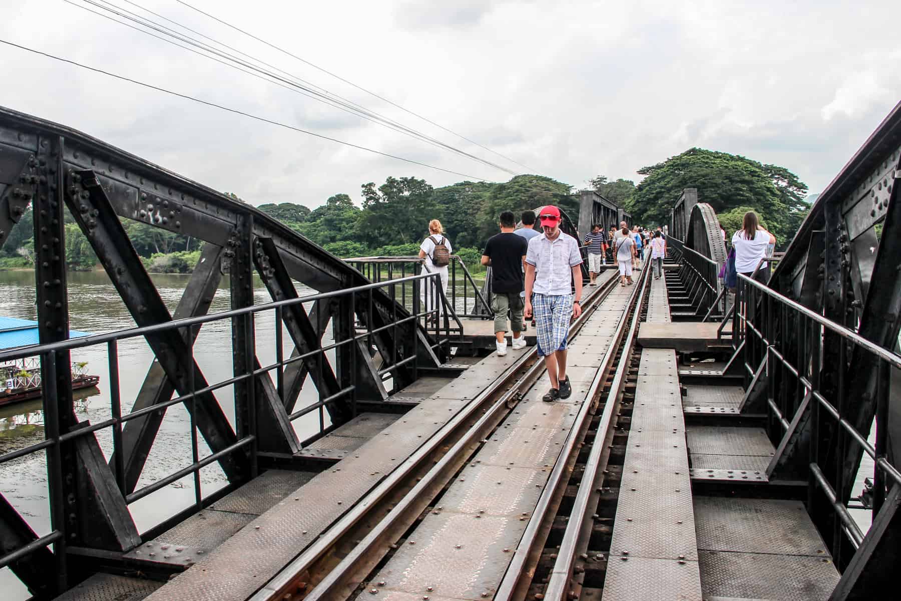 Tourists visiting the Bridge over the River Kwai in Thailand, walking on the Death Railway track and standing on the viewpoint ledges.