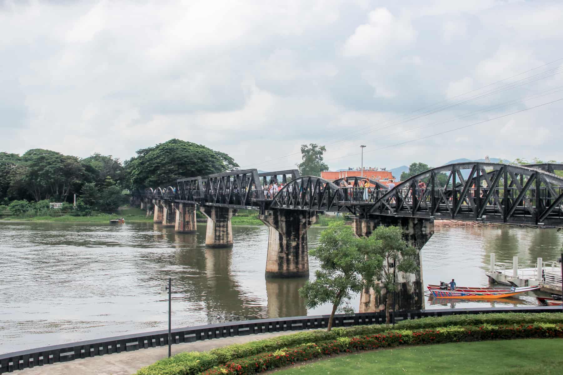 The black iron railings of the Bridge over the River Kwai in Kanchanaburi, Thailand, backed by forest green