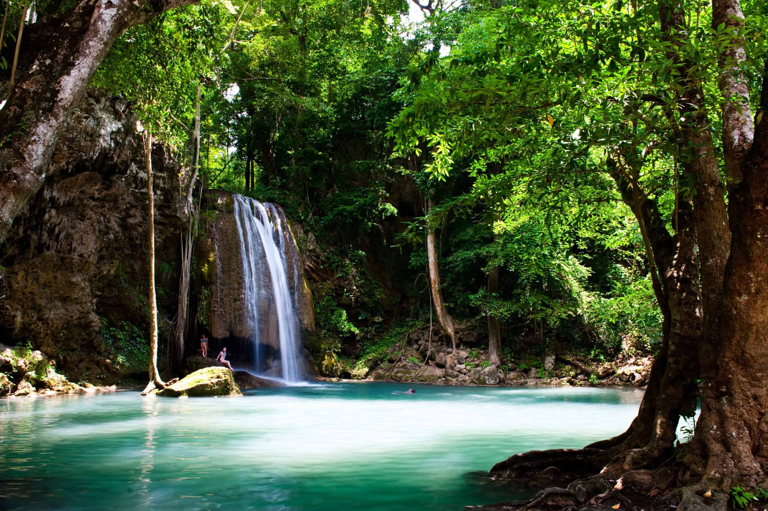 A person swims by one of many waterfalls in Kanchanaburi that flow into bright blue waters in Erawan National Park.
