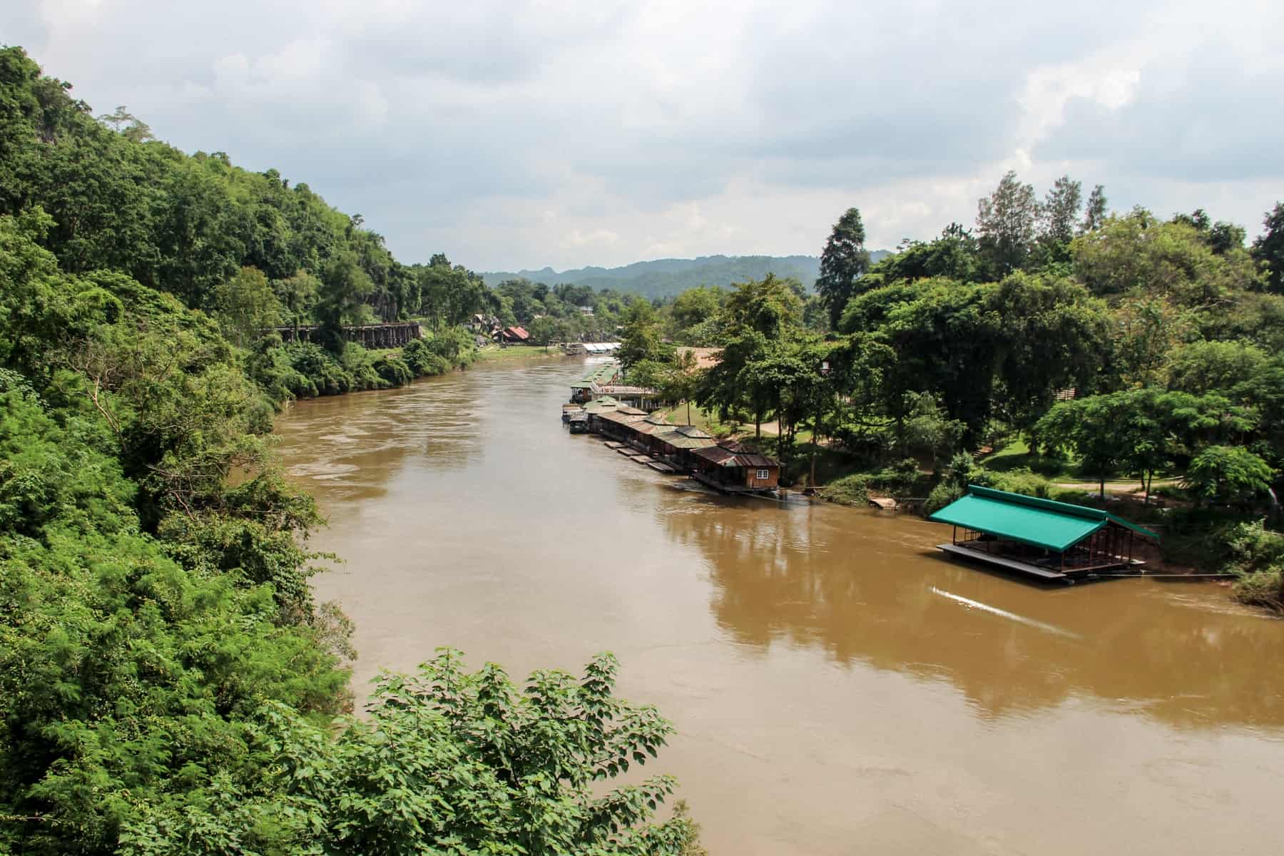 The brown river with floating huts and jungle green valley in Kanchanaburi Province in Thailand.