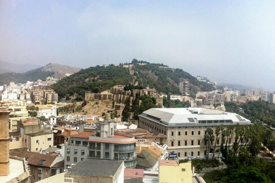 Ariel view of Malaga's golden castle ruins perched on a hilltop in the middle of a valley full og white and beige houses.