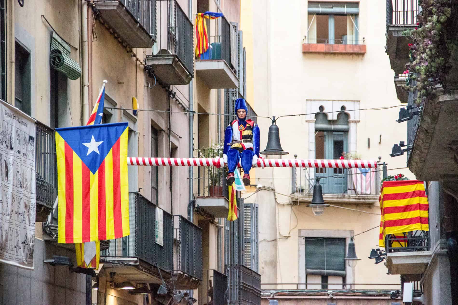 A jester figure dressed in blue and four Catalonia flags hangs from balconies in Girona city, Spain.