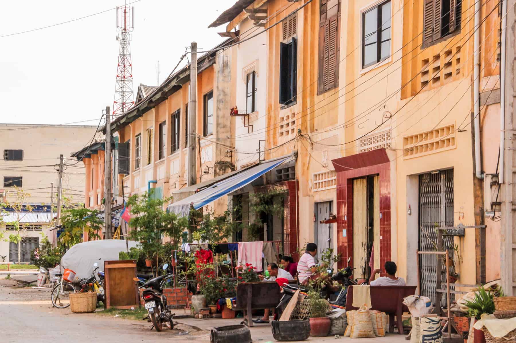 Kampot locals sitting outside a French colonial style row of houses in striped hues of yellow and orange.
