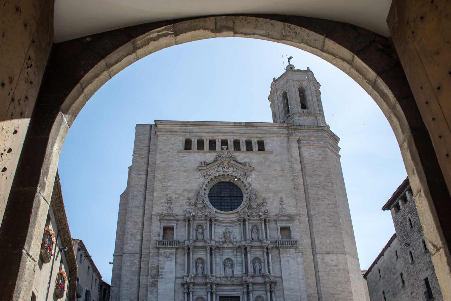 A golden stone archway frames a dusty white Cathedral, with a Gothic facade and a spire on the white hand side. 