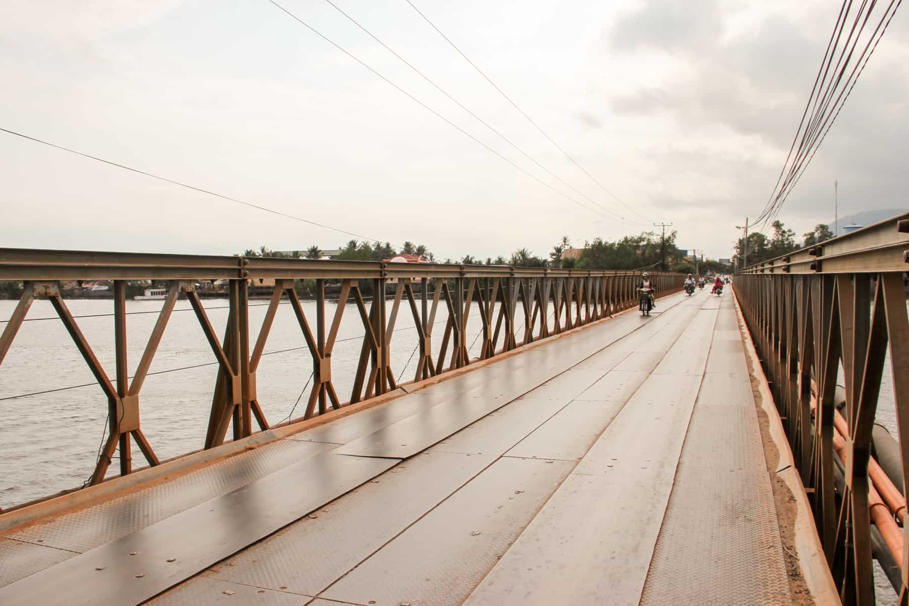 Motorbike approach from a distance on a Iron clad traffic bridge in Kampot that connects two sides of the river below. 