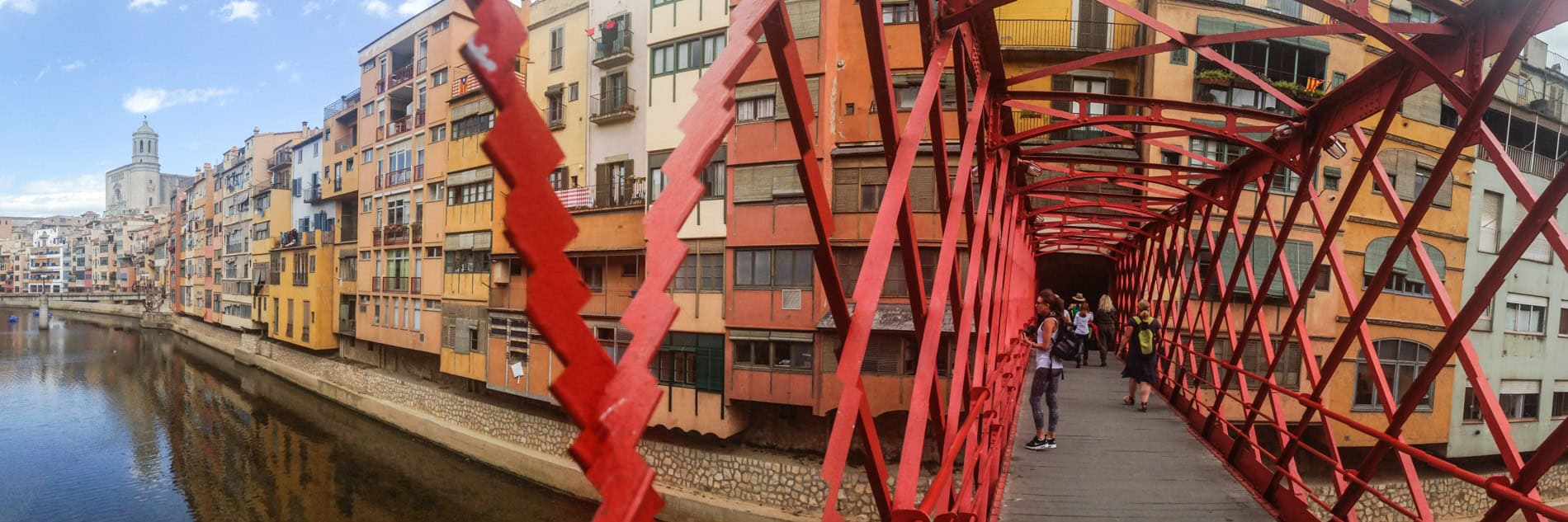 View from the red, metal grates of the Peixateries Velles Bridge in Girona, looking towards a row of colourful buildings. 