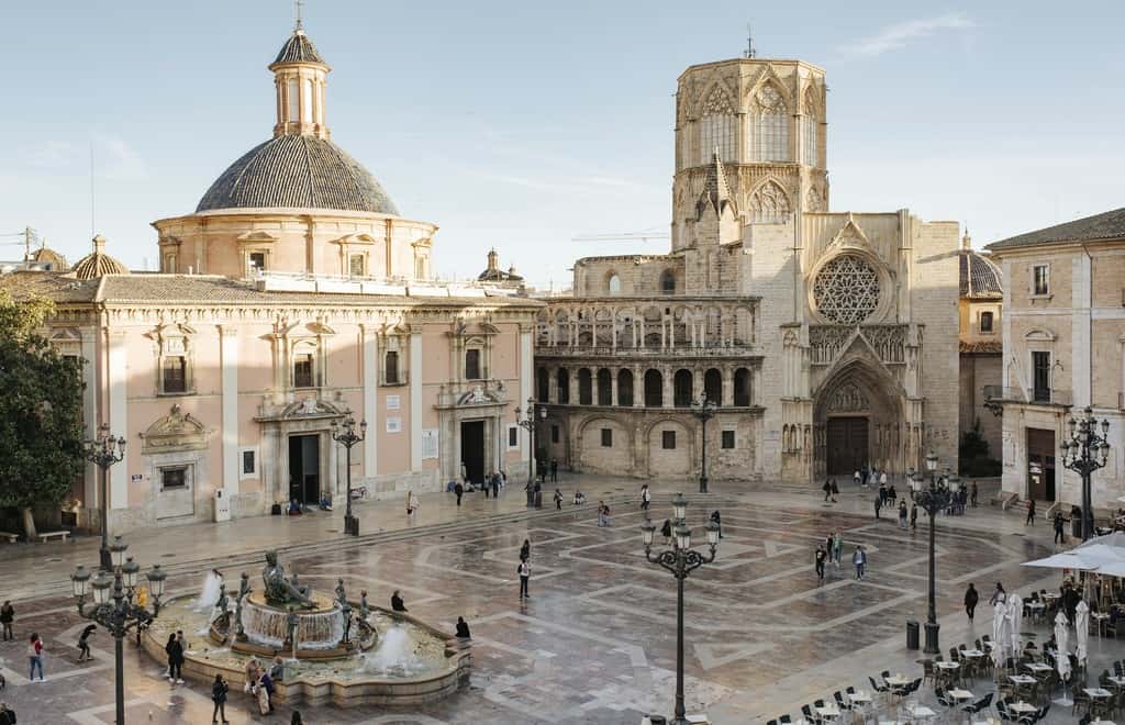 A large square with a golden brown tiled floor and fountain, surrounded by gleaming caramel coloured classic looking buildings in Valencia, Spain