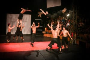 A group of circus performers, standing on a red mat and dressed in black throw two people in the air during an acrobatic performance at the circus in Siem Reap, Cambodia.