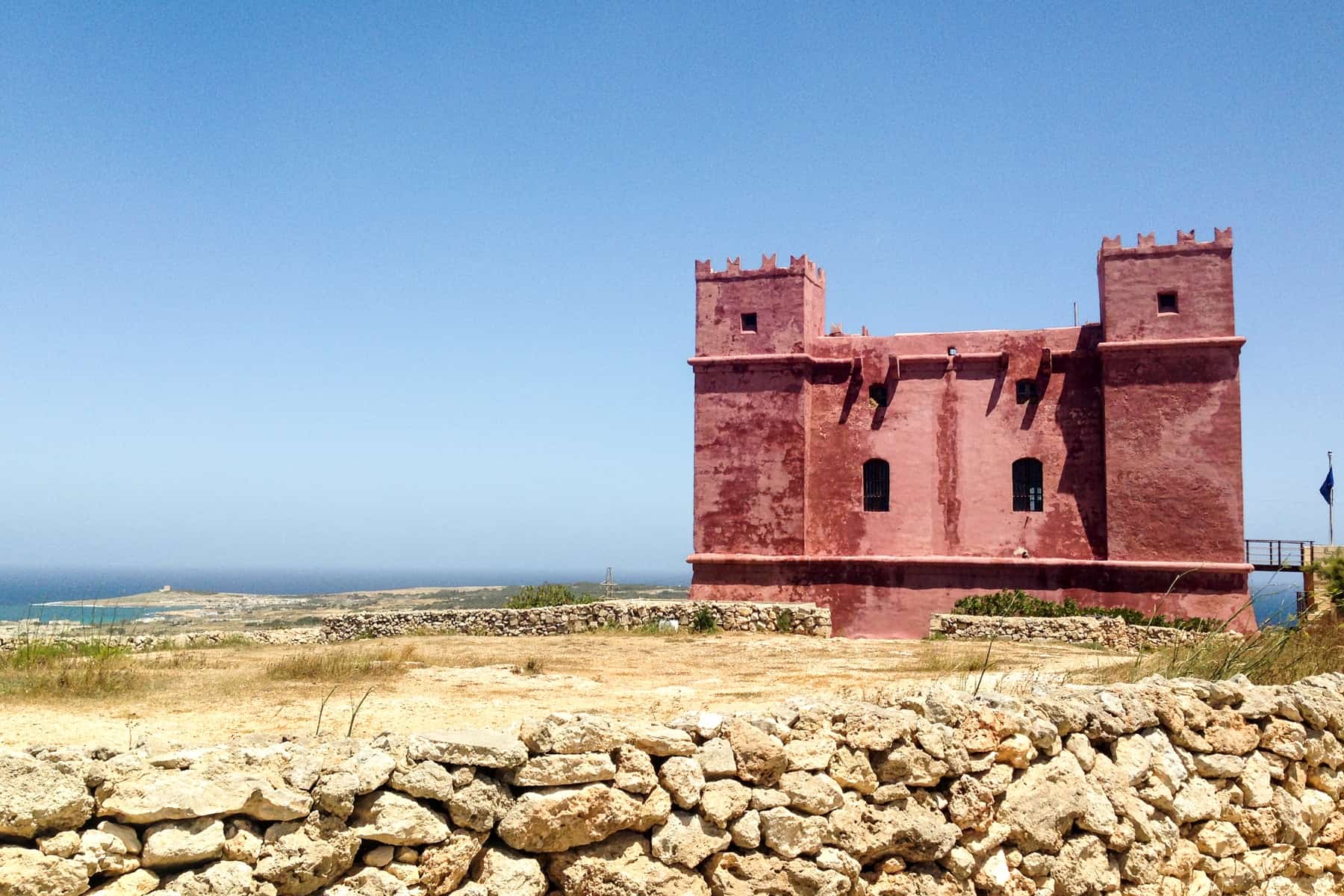 A small red tower with two turrets on a rocky coastline in Malta. 