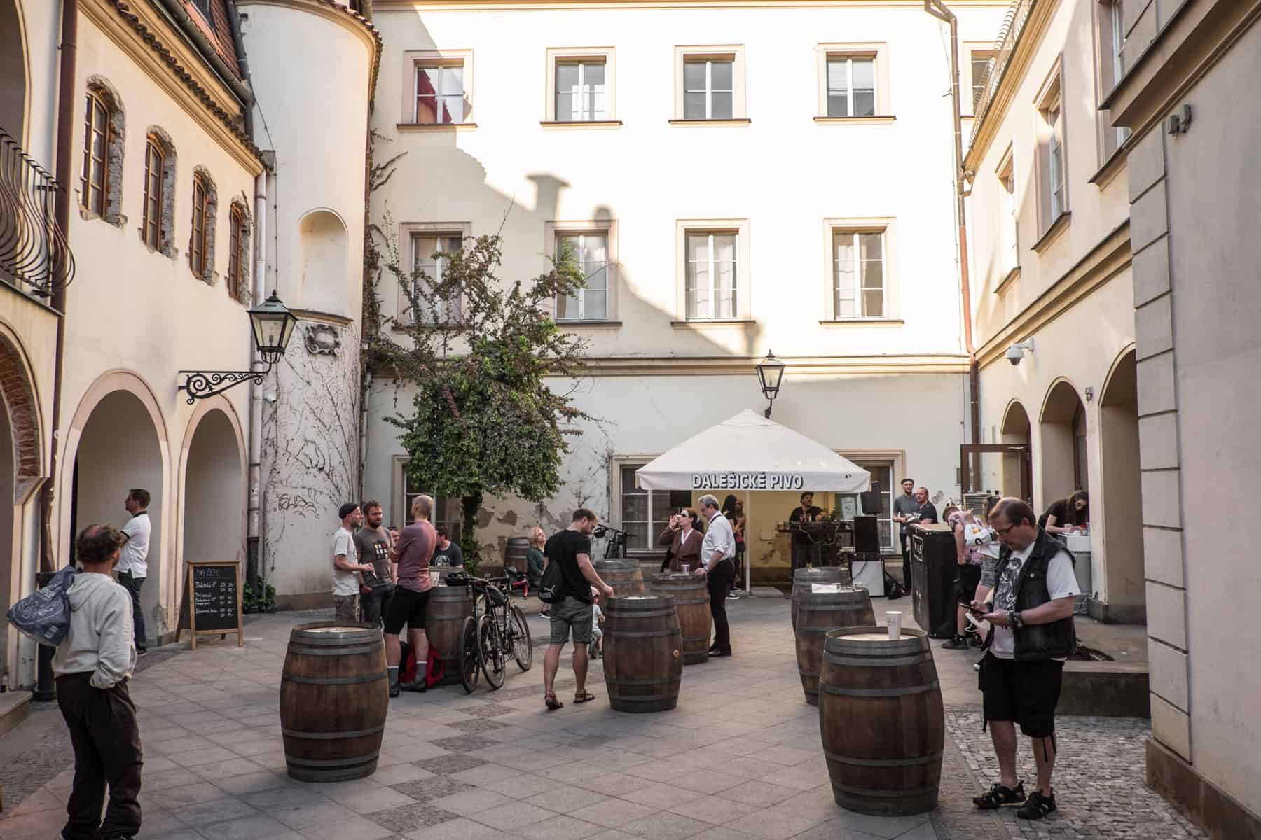 People standing around wooden barrels, drinking at a social gathering in a courtyard in Brno, Czech Republic.