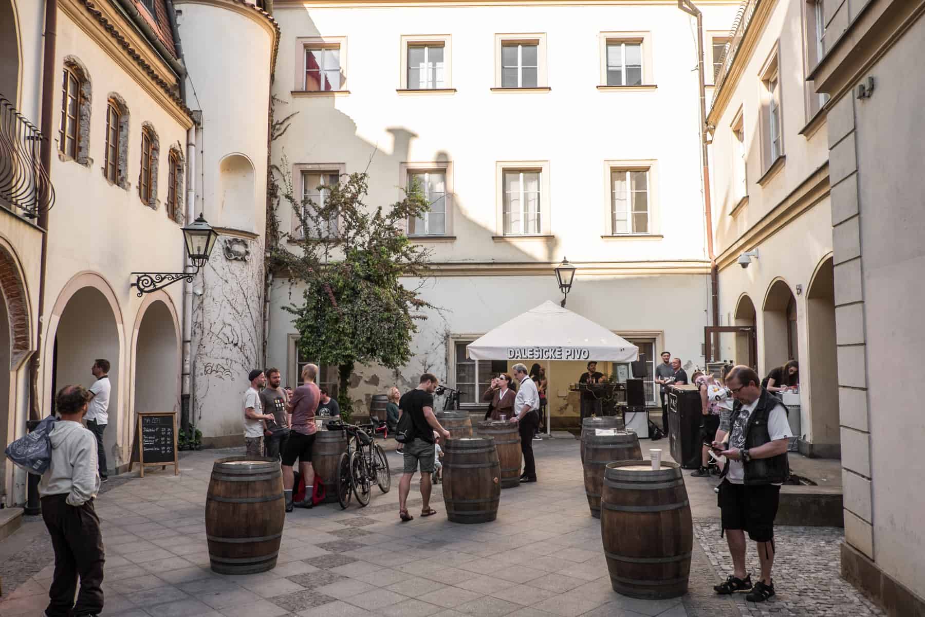 brno places to visit People standing around wooden barrels, drinking at a social gathering in a courtyard in Brno, Czech Republic.
