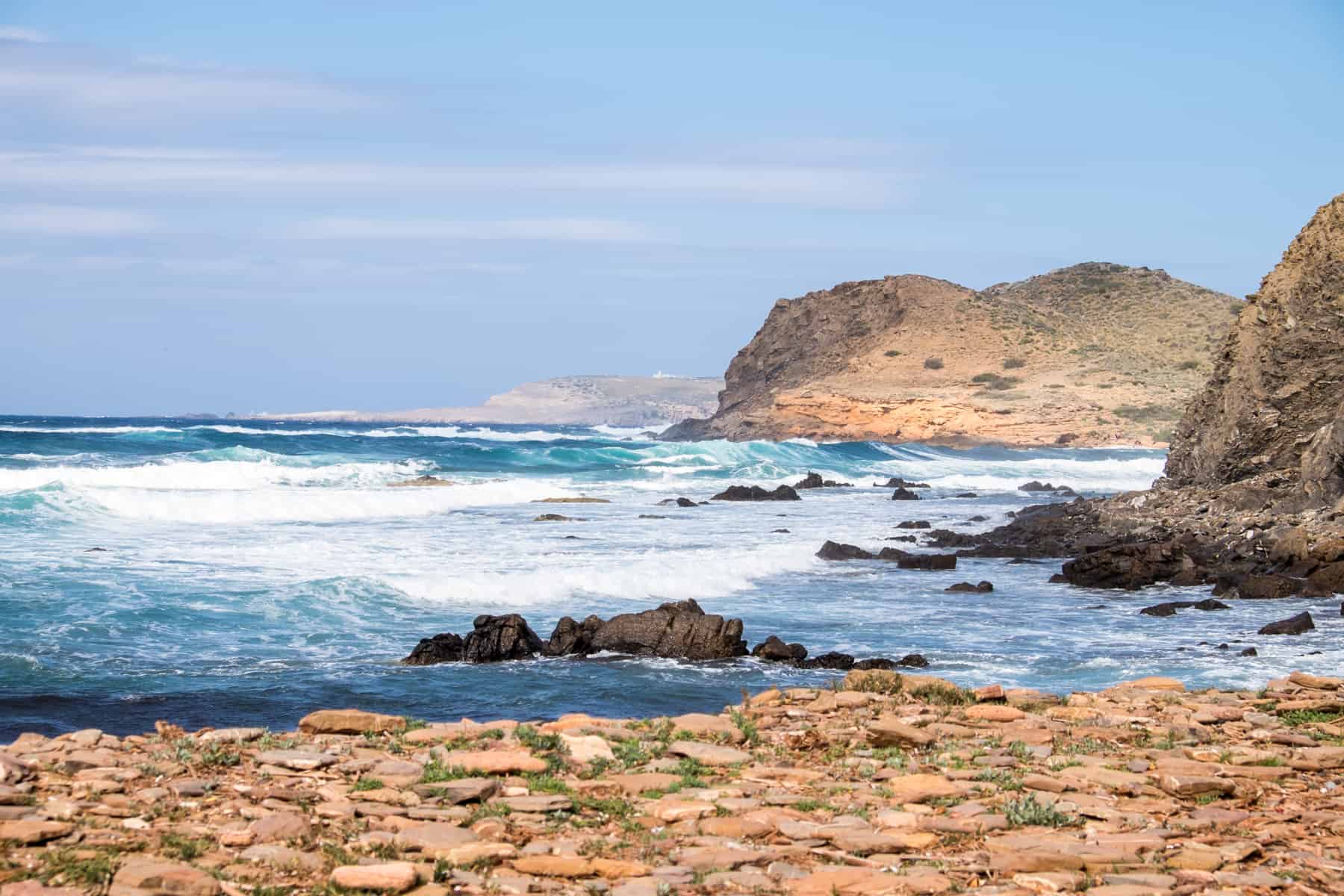 White Crashing waves from deep blue waters break on the golden rocky coastline of Menorca, Spain. 