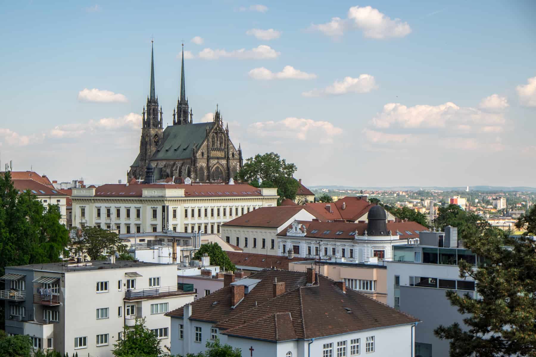 Elevated view of Brno city with red roofed buildings and a hilltop church.