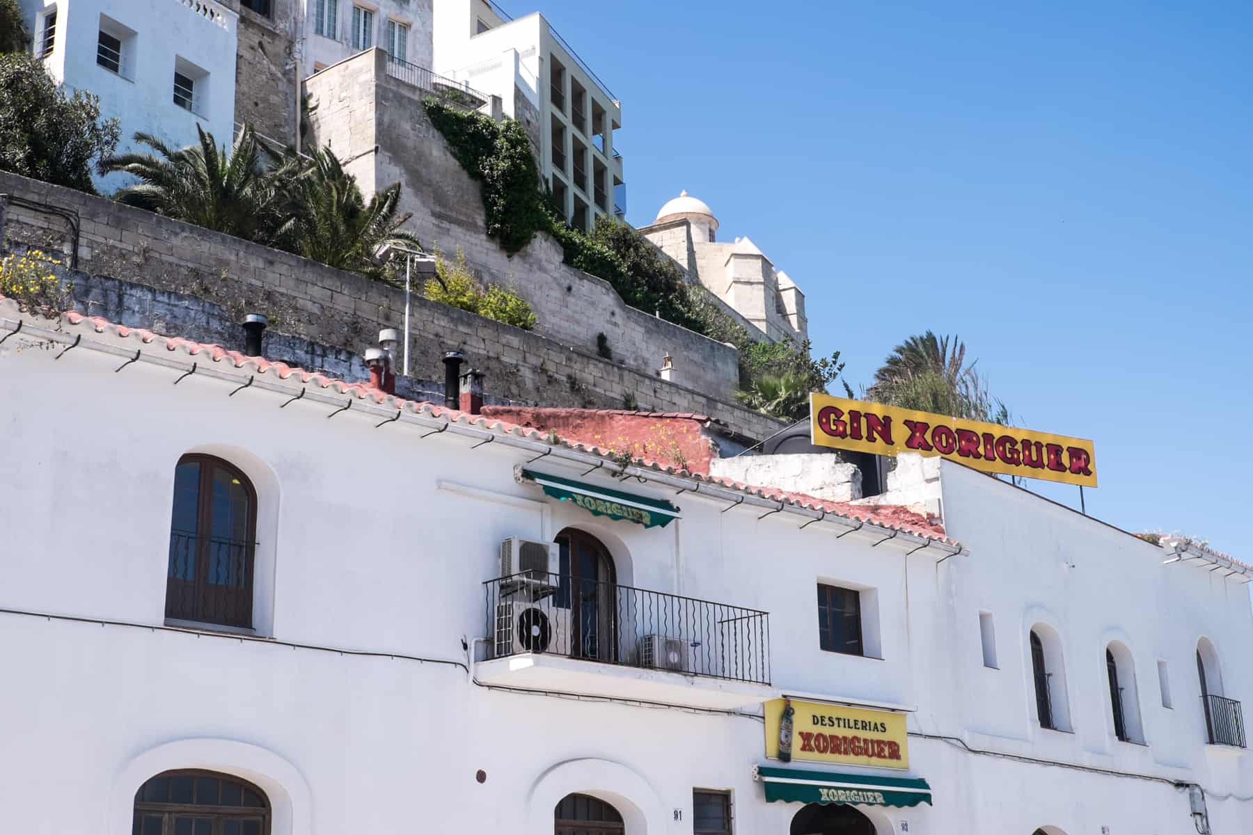 A long white building with the signs 'Gin Xoriguer' and 'Distilerias' in Menorca, Spain.