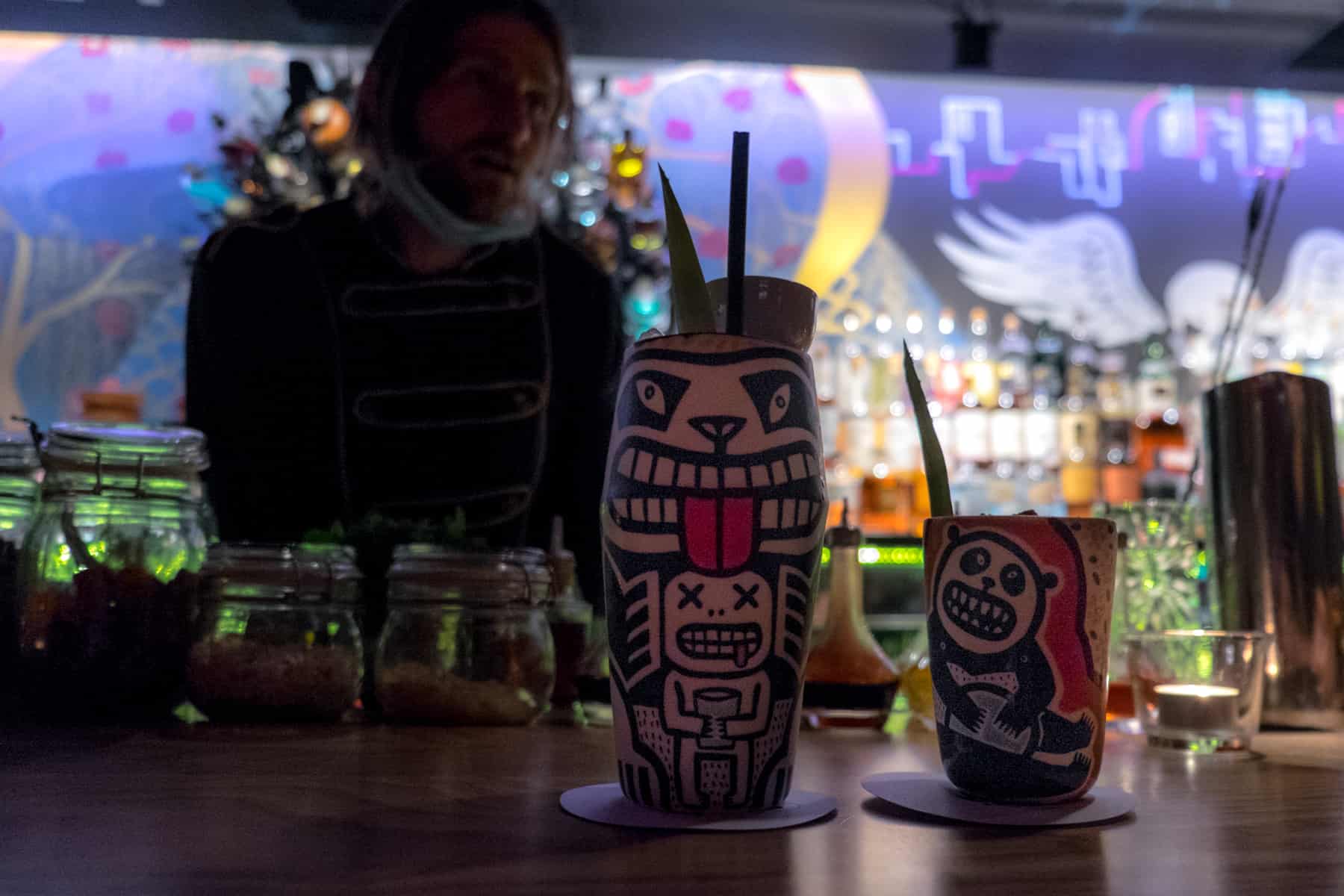 A barman stands behind two cocktails in panda artwork classes, at the funky decorated Super Panda Circus bar in Brno.