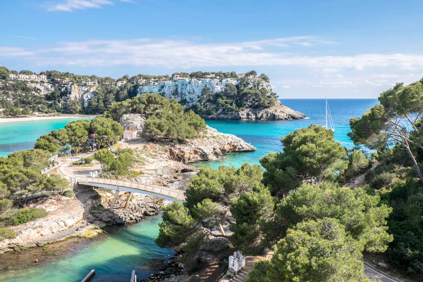 A turquoise cove full of golden rock formations covered in bushy green trees - one of the beautiful bays in Menorca Island, Spain.