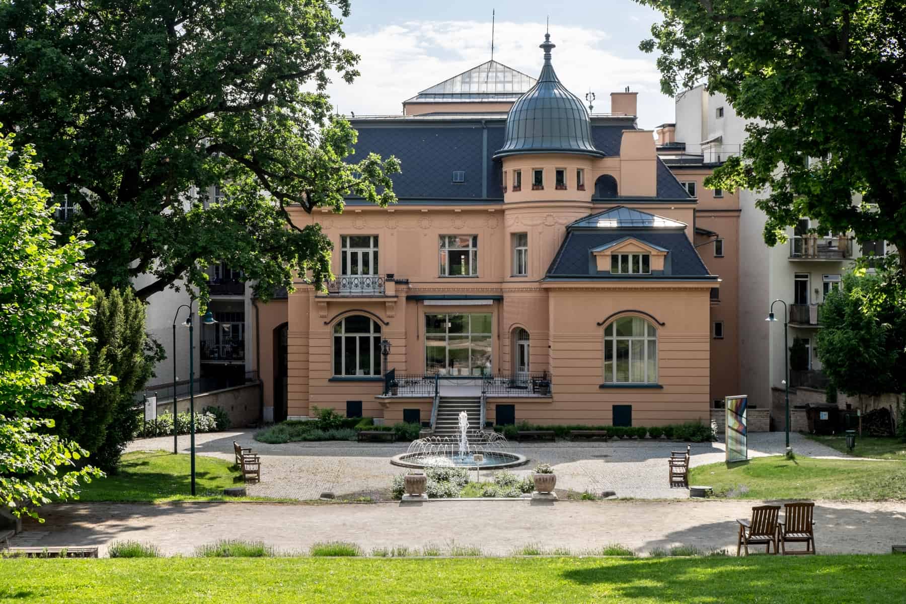 A small garden and fountain in front of the caramel coloured, silver roofed, art nouveau style Löw-Beer Villa in Brno, Czech Republic. 