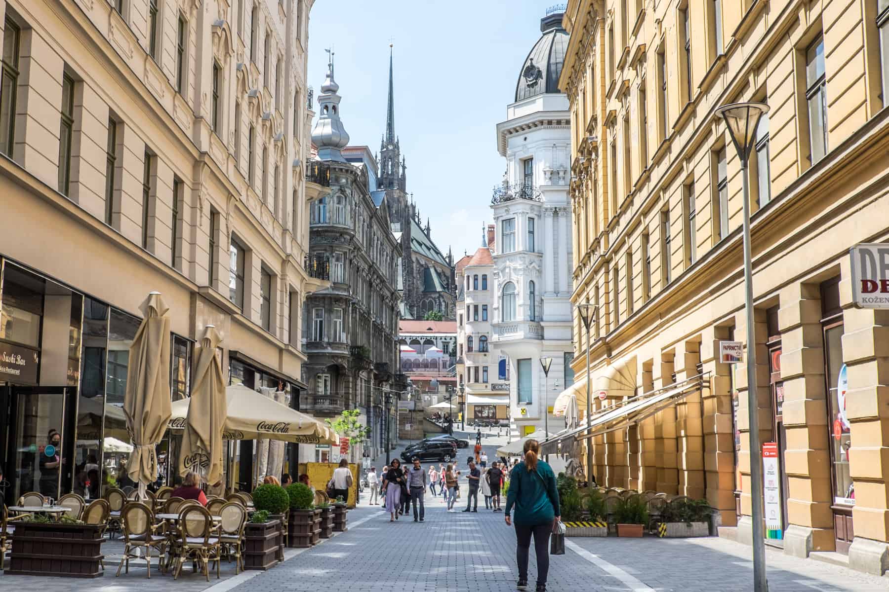 A view down a wide street lines with golden yellow buildings towards a collection of buildings and a cathedral in different colours and architectural types. 