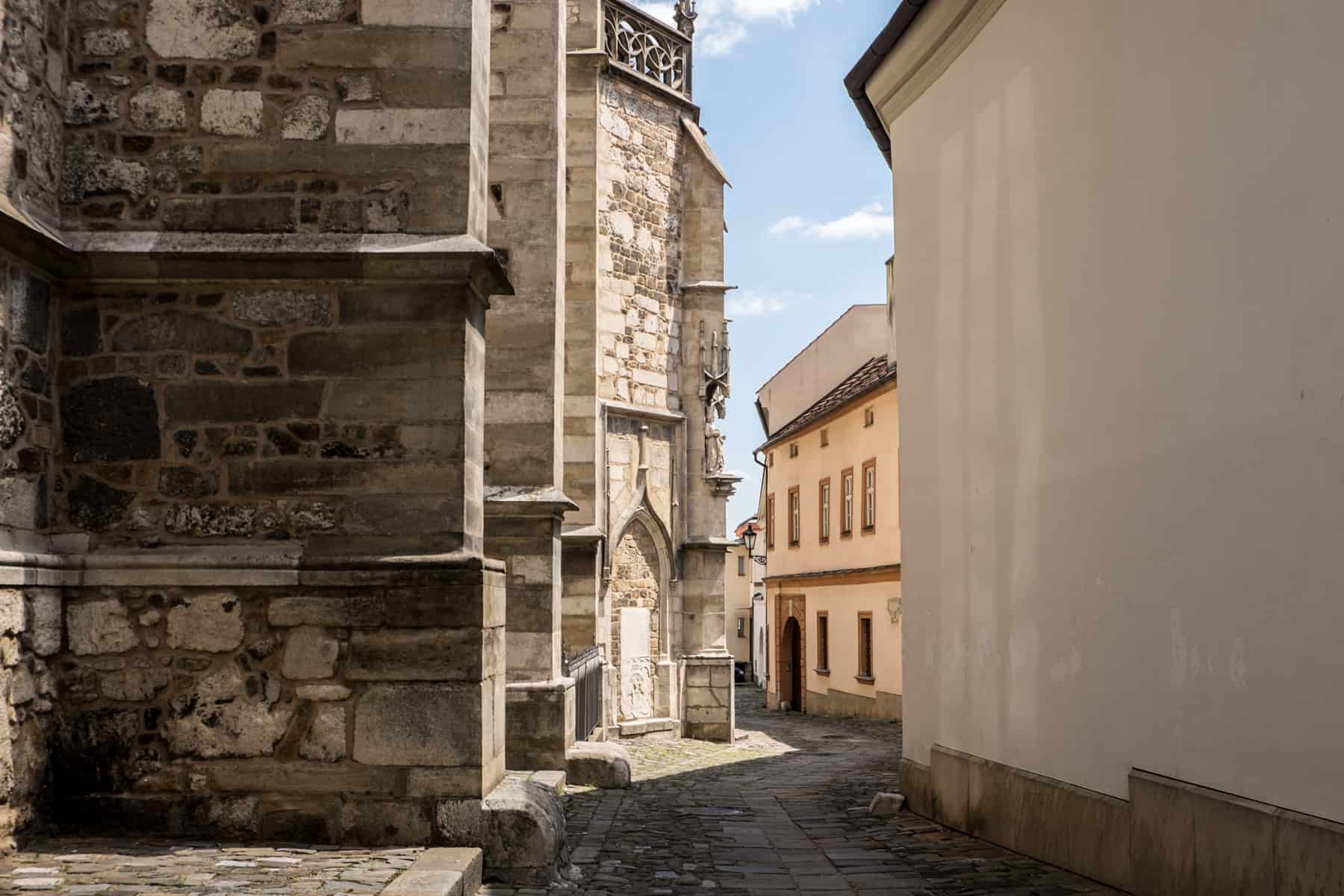 The cobblestone streets next to the old stone Cathedral of St James and St Paul (left) and old low-rise buildings (right) in Brno. 