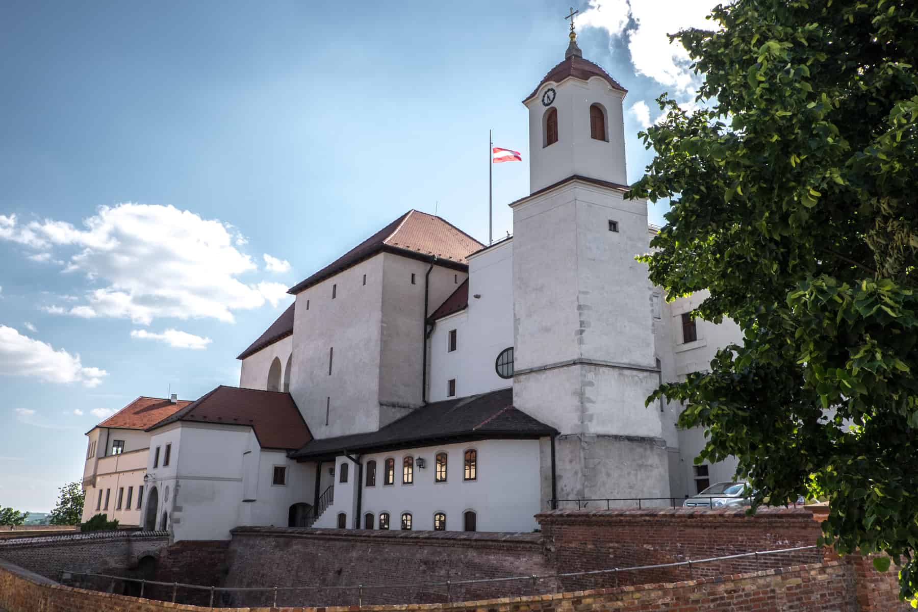 A white medieval castle complex with a red roof and a raised Czech Republic flag.