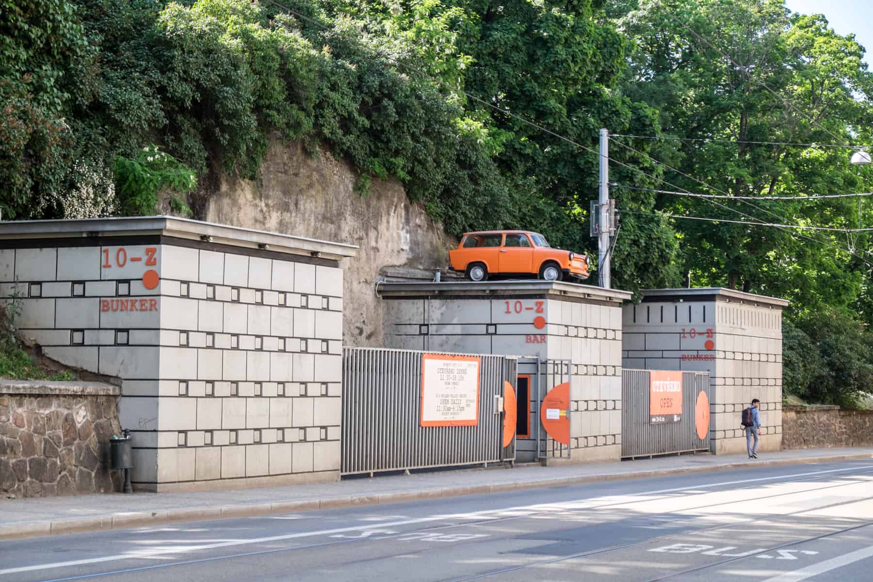 brno places to visit An orange Trabi car on top of one of three square, concrete blocks - the entrance to the 10-z bunker in Brno.