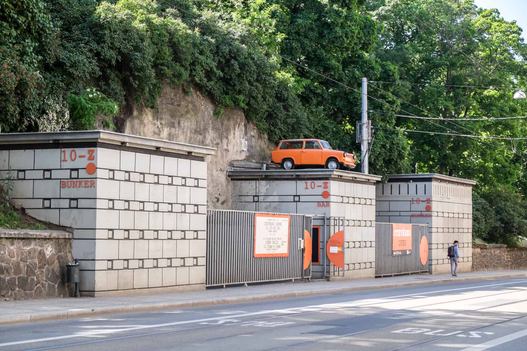 An orange Trabi car on top of one of three square, concrete blocks - the entrance to the 10-z bunker in Brno.