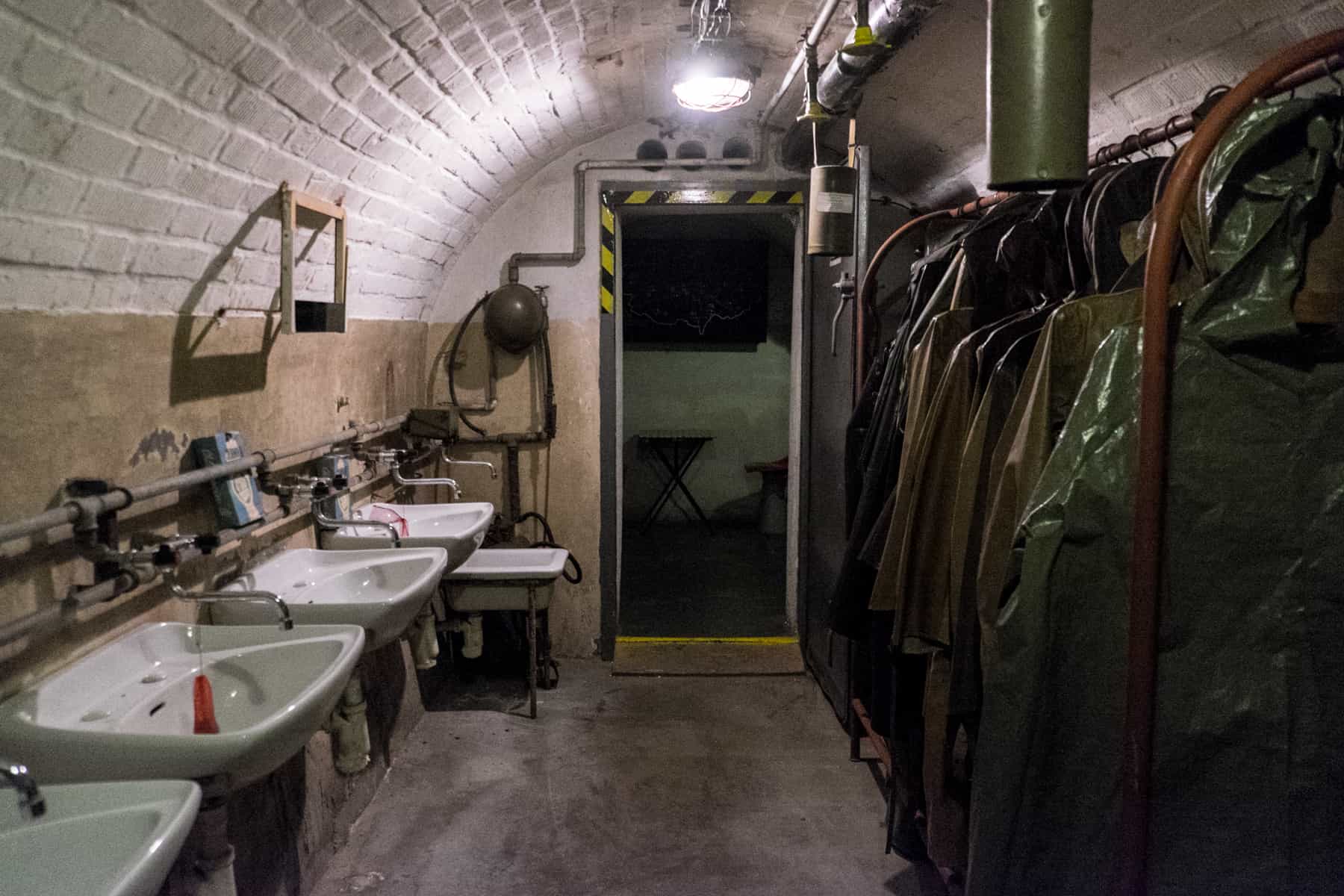 White sink to the left and opposite, a rack of army green coats designed for nuclear attack in a bunker room in Brno city. 