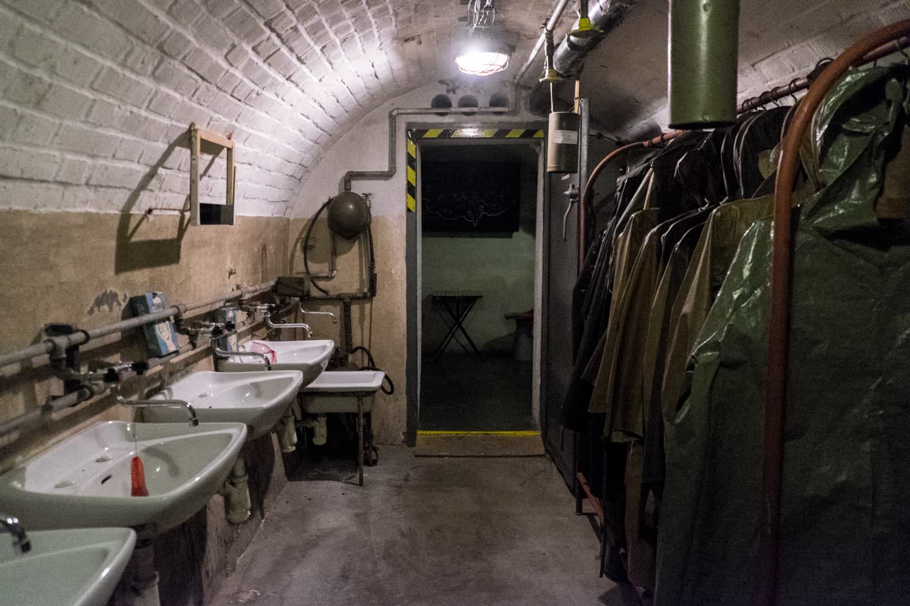 brno places to visit White sink to the left and opposite, a rack of army green coats designed for nuclear attack in a bunker room in Brno city.