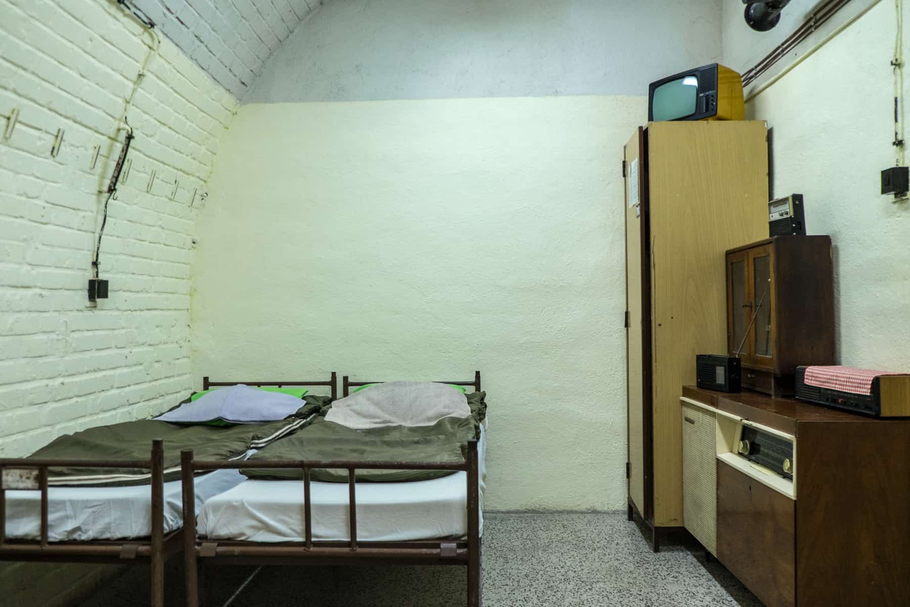 Two iron frame beds with green sleeping bags, and a selection of dated wooden furniture - a double room at the 10-Z bunker in Brno, a former nuclear fallout shelter. 