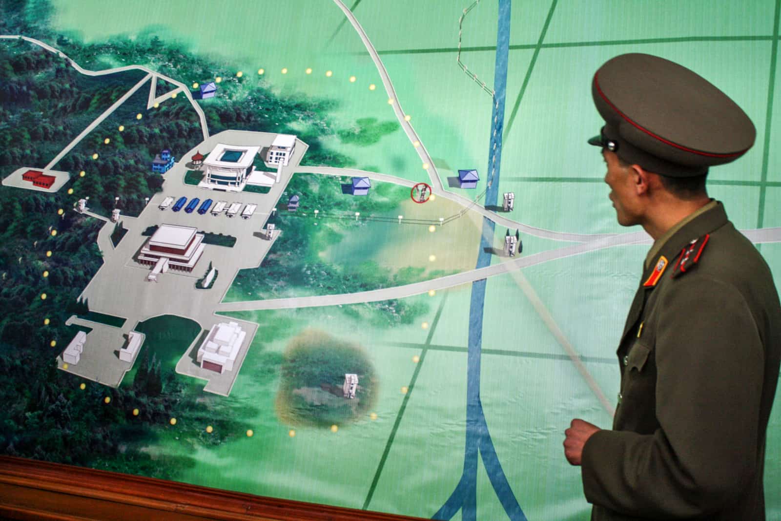 A member of the North Korean Military stands next to an image detailing the DMZ and JSA area that borders the two Koreas. 