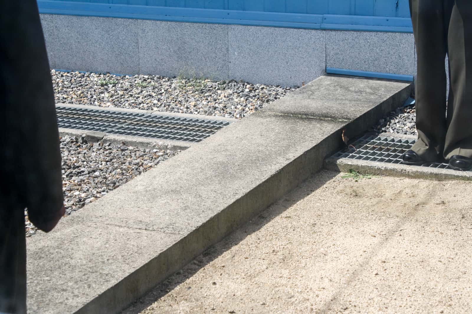 The feet of a North Korean guard standing next to the long concrete block DMZ Military Demarcation Line at Panmunjom, Korea.